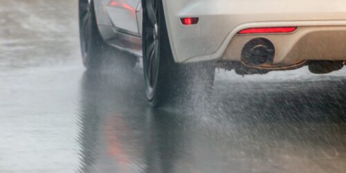 A photo of a car driving on pavement in the rain.